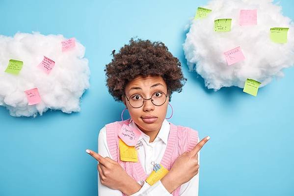 puzzled-hesitant-skilled-female-business-worker-poses-around-colorful-reminder-stickers-hesitates-two-options-wears-round-spectacles-isolated-blue-wall