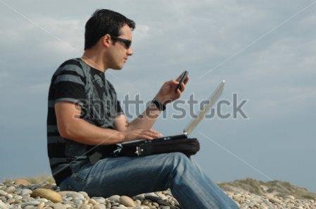 stock-photo-a-young-man-sited-on-the-beach-working-with-a-laptop-and-with-mobile-phone-31283947