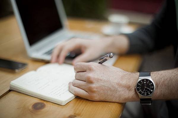 man-writing-in-notebook-with-laptop-in-background.jpg